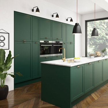 dark green modern kitchen with black light fixtures and herringbone wood flooring