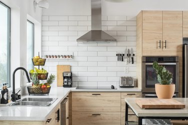 corner of kitchen with large windows, subway tile wall, pale wood cabinetry