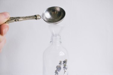 Pouring a tablespoon of vodka into glass bottle with lavender inside