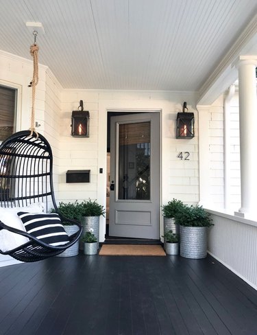 Craftsman front porch with hanging black chair and black lantern wall sconces