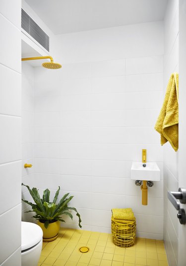 white tiled bathroom with yellow floor and yellow fittings
