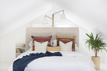 Boho pillows on bed with cream fabric headboard, and plant