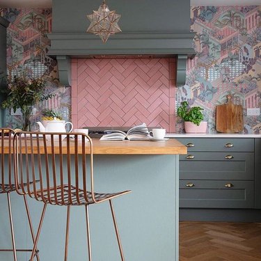 pink pastel herringbone backsplash and muted cabinets with patterned wallpaper