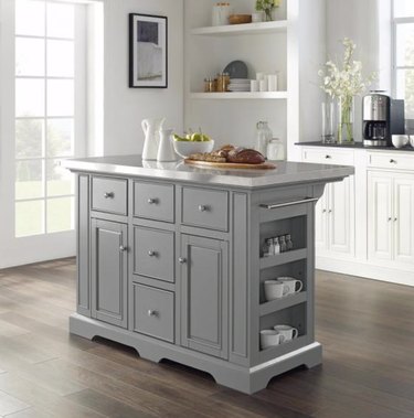 Gray moveable kitchen island in kitchen with white cabinets and wood floors.