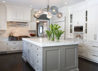 Kitchen with white cabinets, marble backsplash, kitchen island with gray cabinets. Modern glass chandelier.