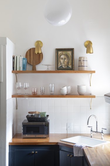 Open shelving in kitchen with brass sconces and wood countertop