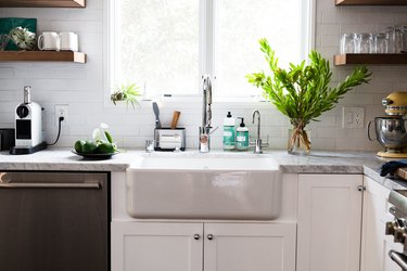 focus on farmhouse sink next to white countertop with large plant and sunny windows