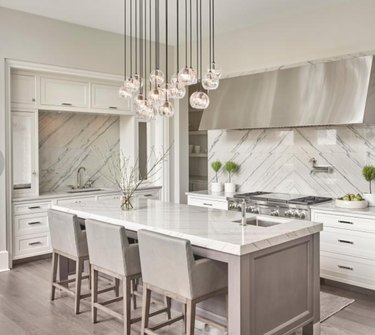 Gray kitchen island with matching gray bar stoops and marble counters. Contemporary chandelier.