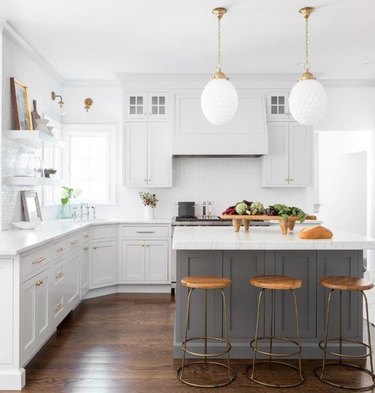 Kitchen with white cabinets and counter tops, hardwood floors, gray kitchen island and white pendant lamps.