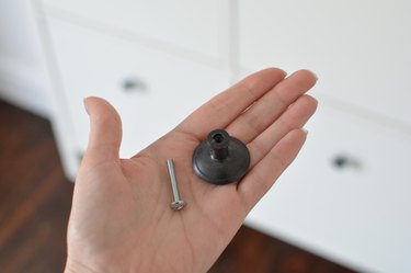 Hand holding metal bolt and black IKEA door handle.