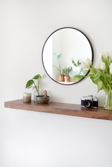 walnut floating shelf vase, white flowers, catch all bowl and circular wall mirror,