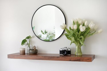 dark brown entryway floating shelf with circular mirror hanging above it.