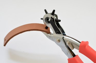 Metal punch pliers making a hole in tan leather