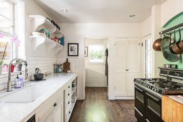 galley kitchen with white walls, white cabinetry, black stove