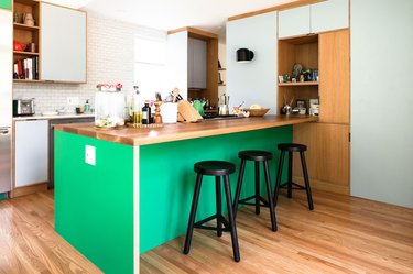 green kitchen island surrounded by mint cabinetry and wood floors and white subway tile walls