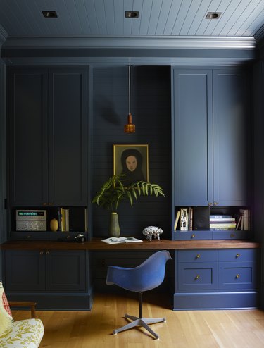 Office with dark blue cabinetry, Eames chair and wood ceiling in blue