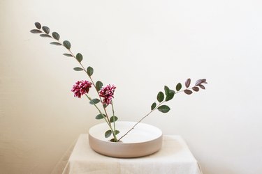 burgundy flowers and two long leaf stems inserted into flower frog inside shallow bowl