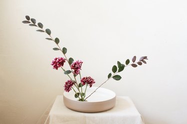 burgundy flowers and two long leaf stems inserted into flower frog inside shallow bowl