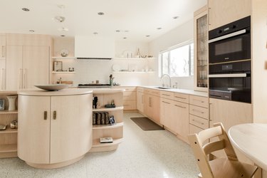 large kitchen with pale wood cabinets, round island, tile floor
