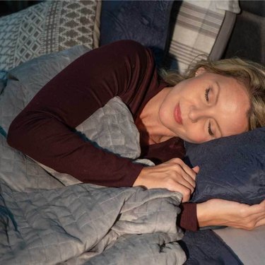 woman sleeping with a gray blanket and a few pillows nearby
