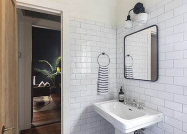 small bathroom with subway tile walls, doors open to dark living space with large palm tree