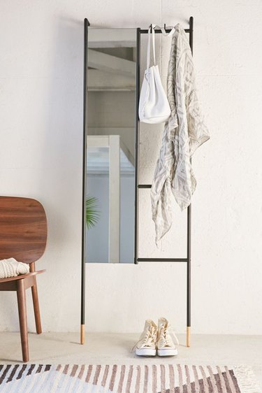 Leaning bedroom mirror from urban outfitters with accessories hanging from the rack side next to accent chair
