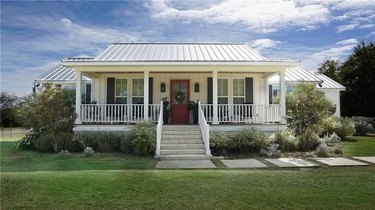 farmhouse style house with white railings and white roof, dark red door