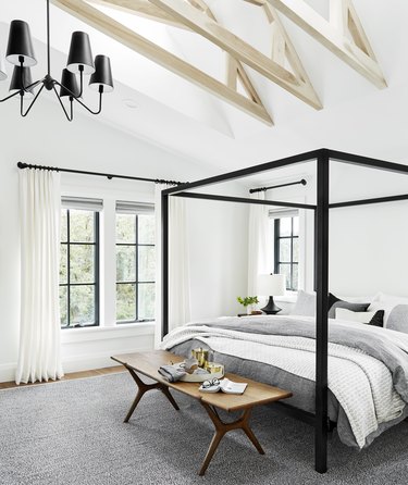 Bedroom chandelier in farmhouse style space with canopy bed and gray linens