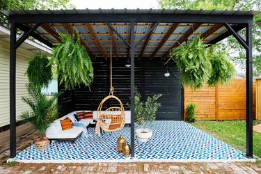 Black and galvanized metal contemporary pergola with hanging ferns and blue floor tiles