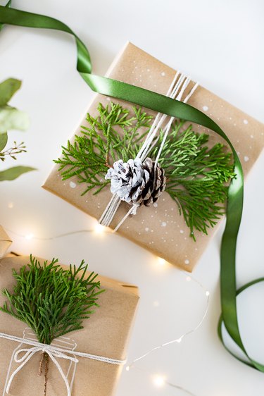 Present wrapped with brown kraft paper and faux greenery with a pinecone