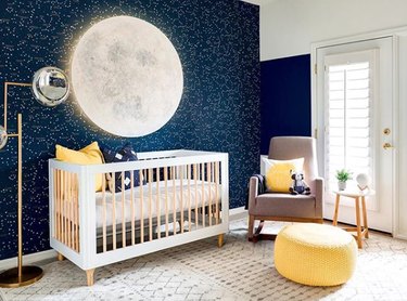 yellow nursery idea with space themed walls and floor pouf by rocking chair