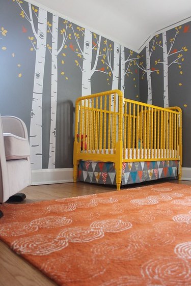 yellow nursery idea with vibrant crib and rust area rug and gray wallpaper