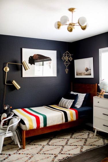 Midcentury kids' bedroom idea with globe-style ceiling light, navy blue walls, and vintage-inspired blanket