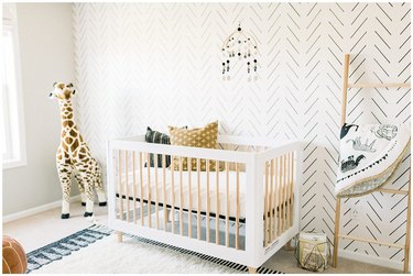 Scandinavian nursery idea with patterned wallpaper accent wall behind crib and leaning blanket rack