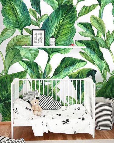 Nursery with palm pattern wallpaper, white crib, black and white quilt.