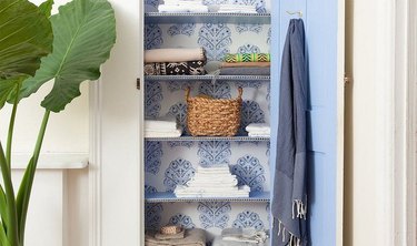 blue and white linen closet idea with patterned wallpaper at back wall and multiple shelves