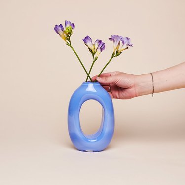 blue vase with hand putting purple flowers inside