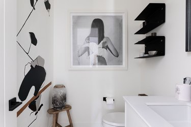 white bathroom, black floating shelves, painting of woman and bird
