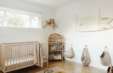 baby nursery design with light wood furniture and surfboard mounted on wall