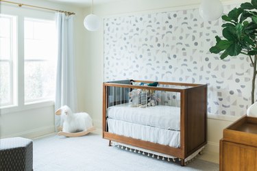 Nursery with geometric pattern wallpaper, modern crib, plant, rug.