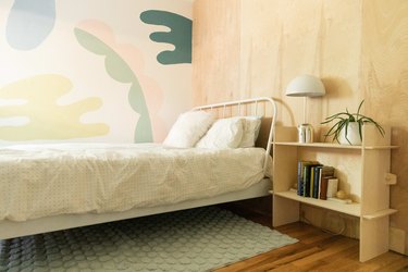 A colorful mural and plywood walls meet in a bedroom.