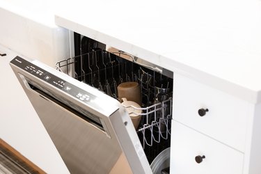 an open dishwasher against white cabinetry with mugs inside
