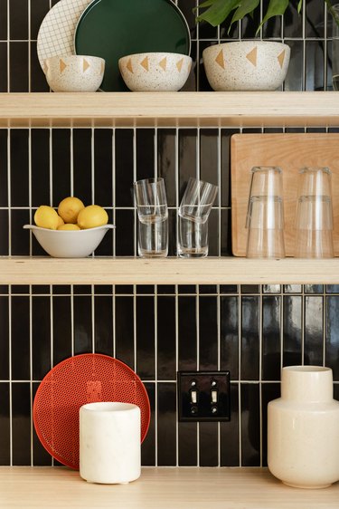 Close up of open shelving and tile work in kitchen, with wood shelves and black tile.