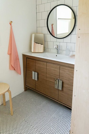 An updated bathroom with large circle mirror and small floor tile.