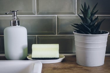Sponge on counter next to sink and soap dispenser