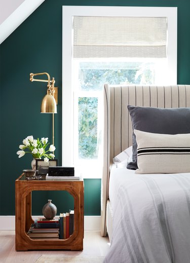 green bedroom with upholstered headboard and brass wall sconces