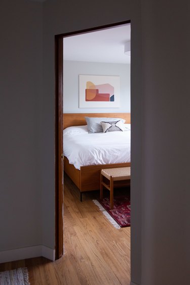 A peek into the master bedroom with wood bed frame and art over bed