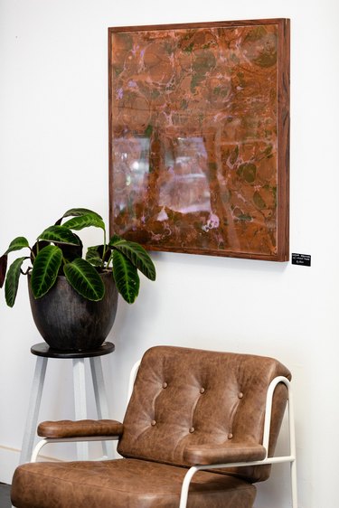 Artwork on wall over leather chair and planter with green plant