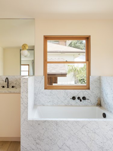 peach minimalist bathroom with marble surround tub and black tub fixtures