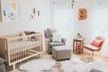 Modern baby nursery idea with wooden crib next to rocking chair by windows